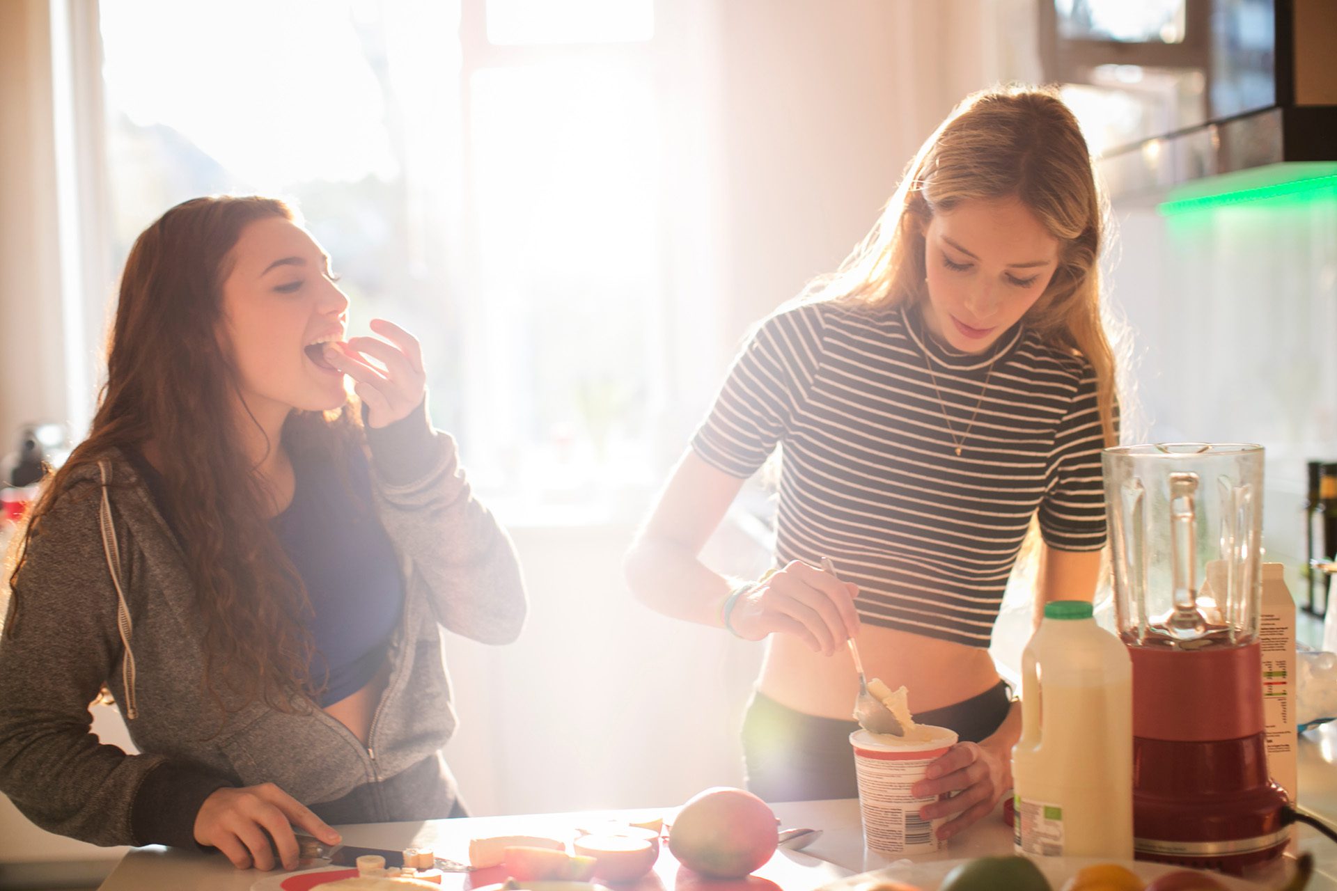 Teenage girls making smoothie in sunny kitchen